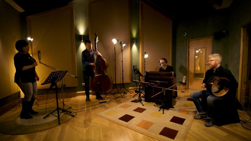 Four musicians recording a track in a music studio.